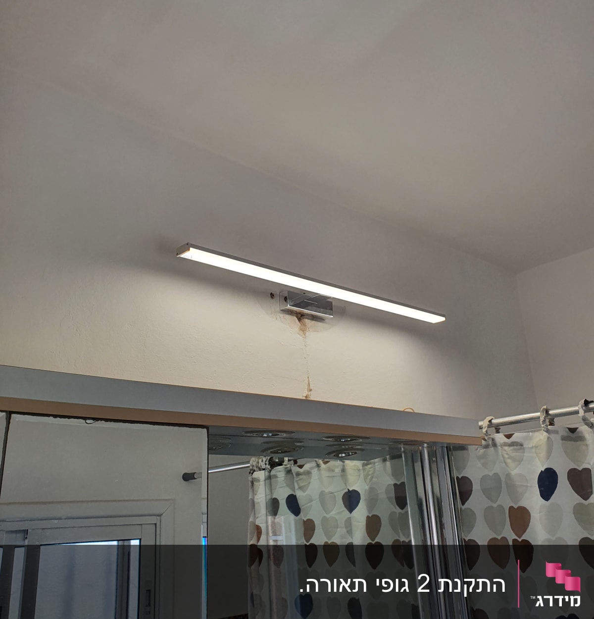 מנורת קיר מותקנת מעל מראה בחדר אמבטיה